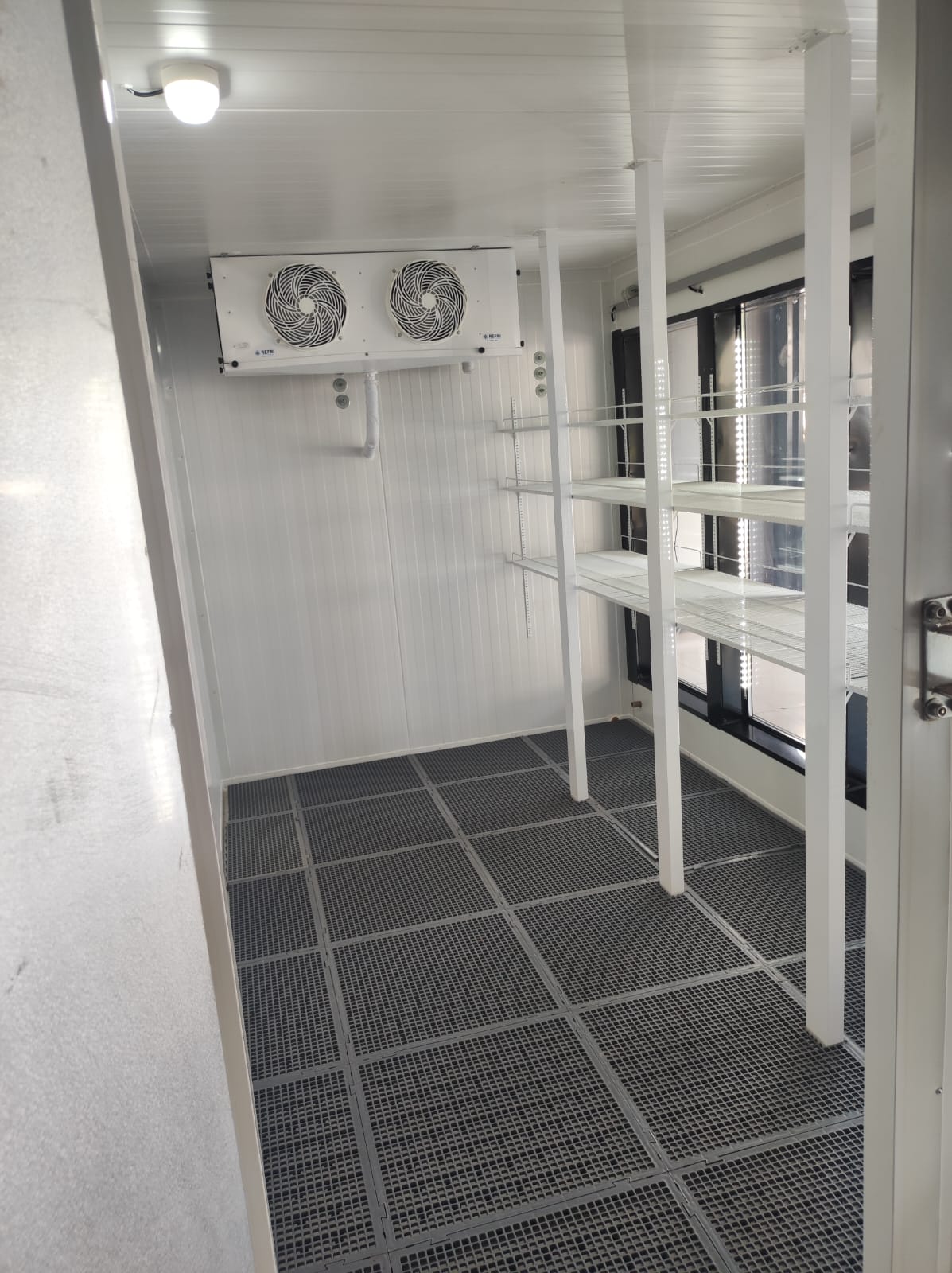 Walk-in cooler com prateleiras internas e sistema de refrigeração.